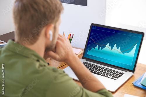 Caucasian businessman sitting at desk, using laptop with statistical data on screen photo