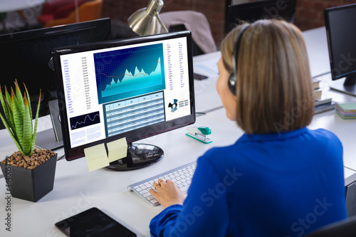 Caucasian businesswoman sitting at desk using computer with statistical data on screen