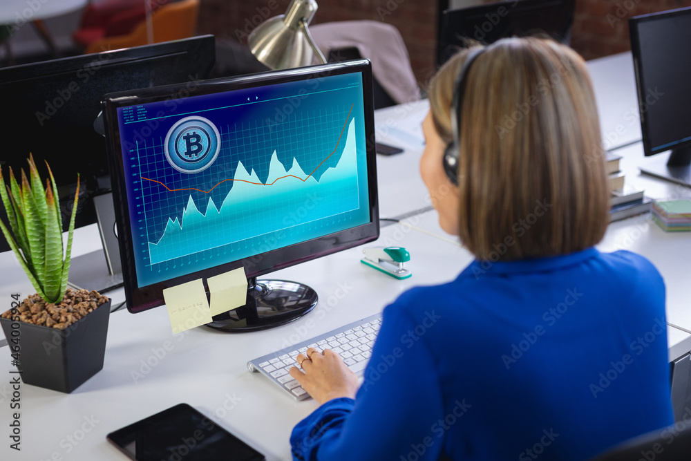 Caucasian businesswoman sitting at desk, using computer with statistical data on screen Caucasian businesswoman sitting at desk, using computer with statistical data on screen