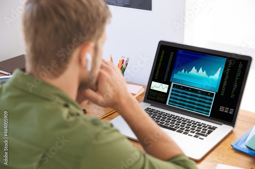 Caucasian businessman sitting at desk, using laptop with statistical data on screen photo