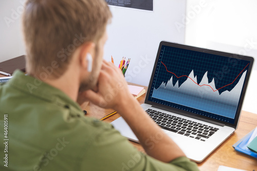 Caucasian businessman sitting at desk, using laptop with statistical data on screen photo