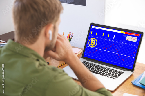 Caucasian businessman sitting at desk, using laptop with statistical data on screen photo