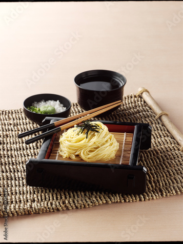 Japanese cold  noodles or Zaru ramen with chopped green onions, grated wasabi and cup for dipping sauce on braided woven rattan jute Placemat on wooden background. photo