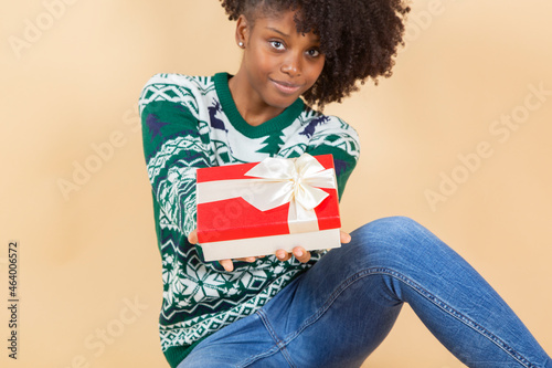 pretty afro american woman with a christmas present, beige background © PintoArt