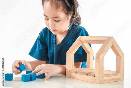 Little girl playing with blue toy blocks and wooden house. A happy kid has concentred to creates constructions with wood bricks. Nursery and childhood educational game for baby and toddler concept photo