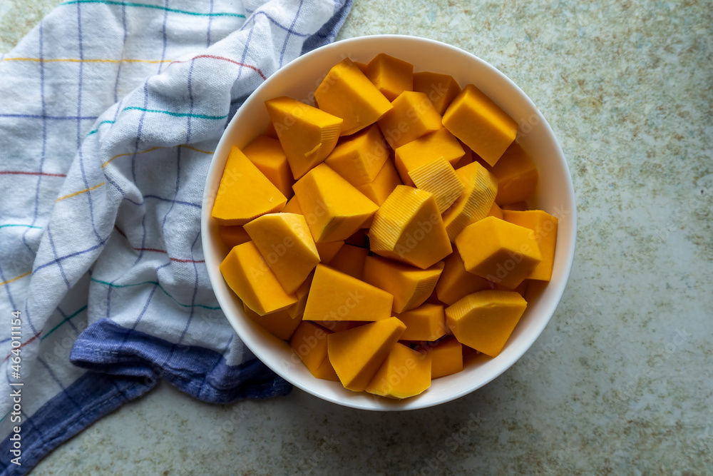 Farmhouse-style cooking, sliced pumpkin in bowl on vintage kitchen old countertop, and thin square lines texture fabric for autumn recipes