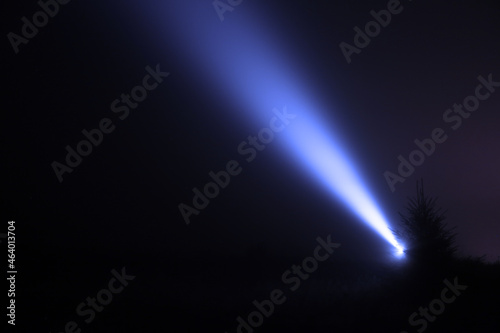 Night sky lit by bright beam of flashlight in forest photo
