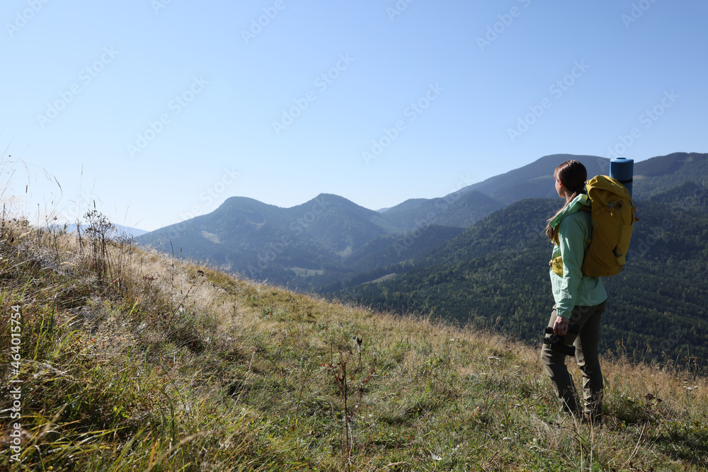 Tourist with backpack and binoculars enjoying view in mountains on sunny day