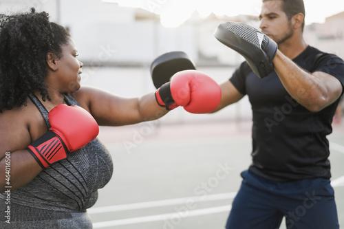 African curvy woman and personal trainer doing boxing workout session outdoor - Focus on left red glove © DisobeyArt