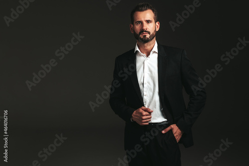 portrait of handsome confident stylish hipster lambersexual model. Sexy modern man dressed in elegant black suit. Fashion male posing in studio on dark background. Looking at camera