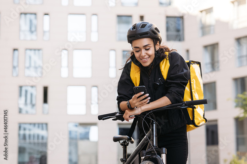 Portrait of a beautiful delivery girl holding her mobile phone while leaning on a handlebar of a bicycle photo