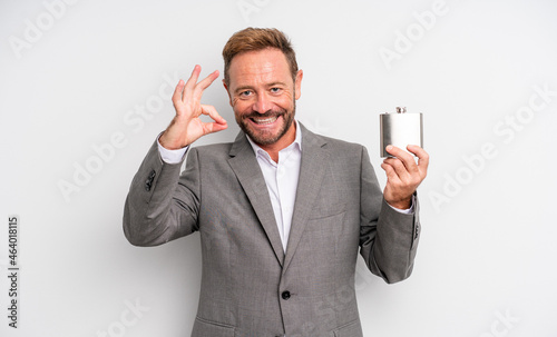 middle age handsome man feeling happy, showing approval with okay gesture. alcohol flask concept photo