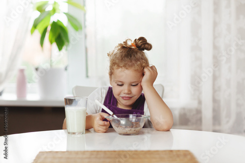 Cute little girl eats cereal with milk for Breakfast. The girl looks thoughtfully at the bowl with . Healthy Breakfast, taking care of children. Space for text