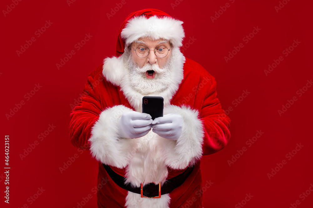 Naklejka premium Photo of funky impressed man pensioner dressed santa claus costume chatting modern device big eyes isolated red color background