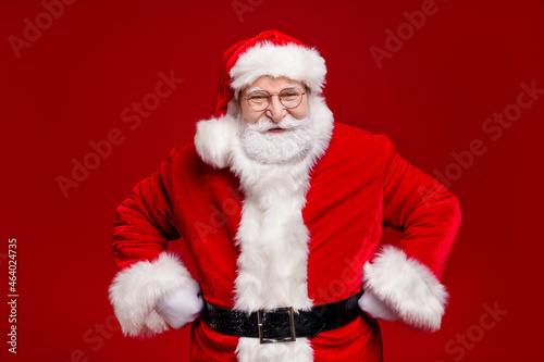 Photo of funny funky retired man wear santa claus costume cap spectacles smiling arms hands waist isolated red color background