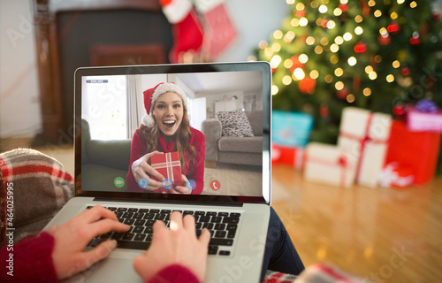 Caucasian woman making christmas laptop video call with smiling female friend holding gift