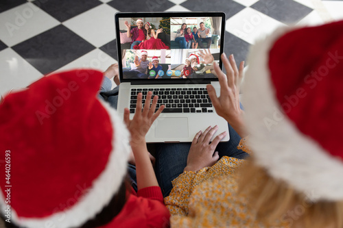 Waving mother and daughter making laptop christmas video call with diverse family and friends