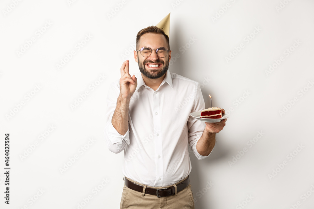 Holidays and celebration. Happy man making wish on birthday cake, cross  fingers and smiling excited, having b-day party, white background Stock  Photo | Adobe Stock