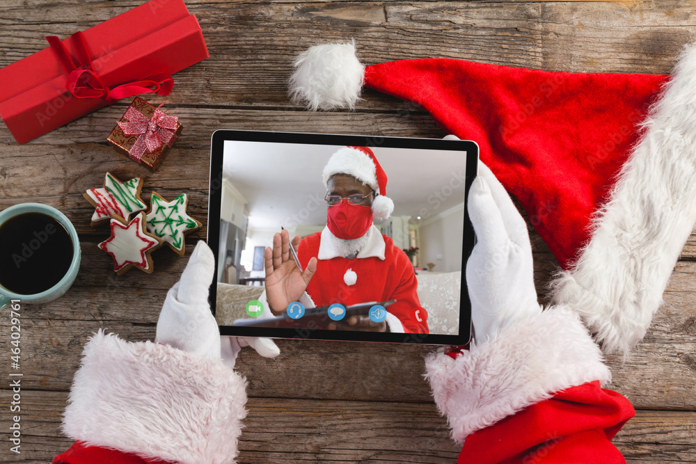 Fototapeta premium Hands of santa claus holding tablet with santa claus in face mask on screen