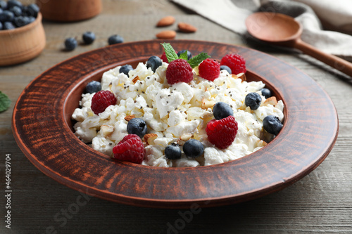 Fresh cottage cheese with berries and mint in plate on wooden table, closeup