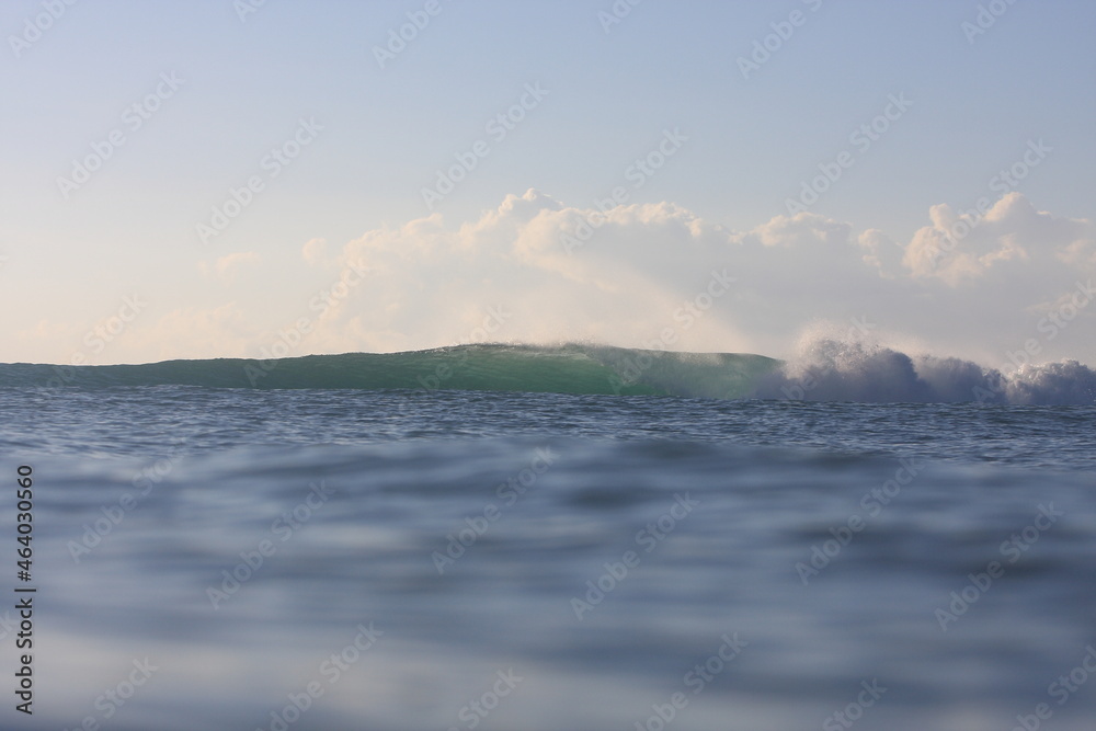 water photo of empty wave breaking in the distance with calm water in foreground and clouds in the sky