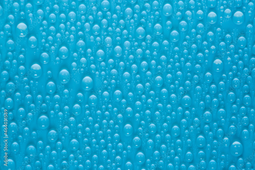 Drops of water on the glass on a blue background. Texture of a water drop as a background. Freshness after the rain. Wet clean nature ecology.