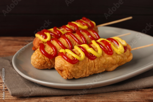 Delicious corn dogs with mustard and ketchup on wooden table, closeup
