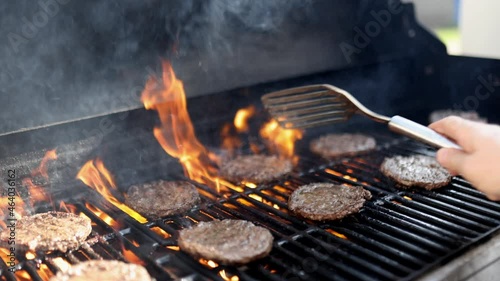 Male hand flipping hamburger meat above the high flame of barbecue grill