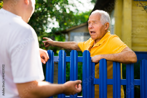 Neighbor conversation. Two smiling men breezily chatting near fence of rural house photo