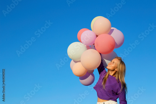 A young Caucasian girl launches a bunch of colorful balloons into the sky. Girl on a background of blue sky smiles and hold balloons.