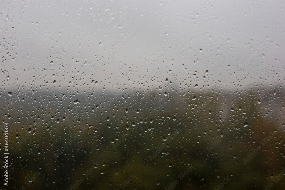 Window with raindrops and blurry view of the autumn forest
