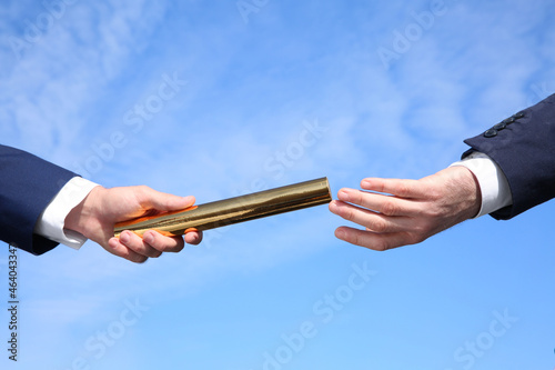 Businessman passing baton to his partner against blue sky, closeup photo
