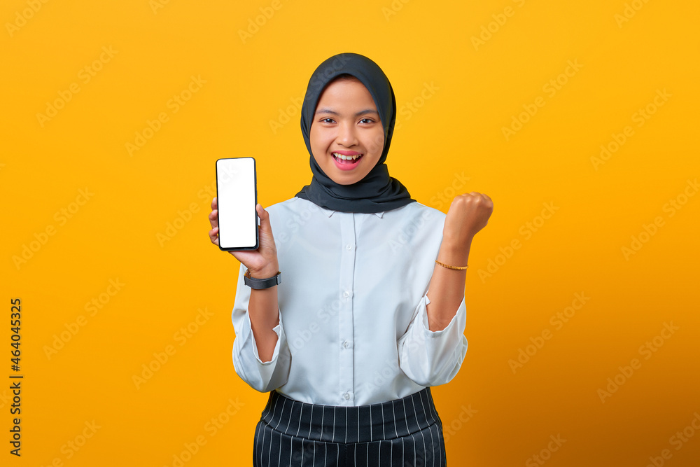 Happy Asian woman showing mobile phone blank screen and hand gesture success on yellow background Happy Asian woman showing mobile phone blank screen and hand gesture success on yellow background