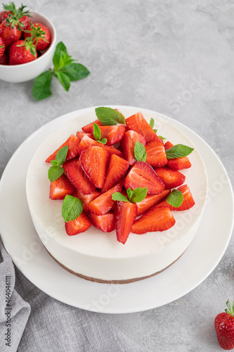 No baked cheesecake with fresh strawberries and mint on top on a white plate on a gray concrete background. Copy space.
