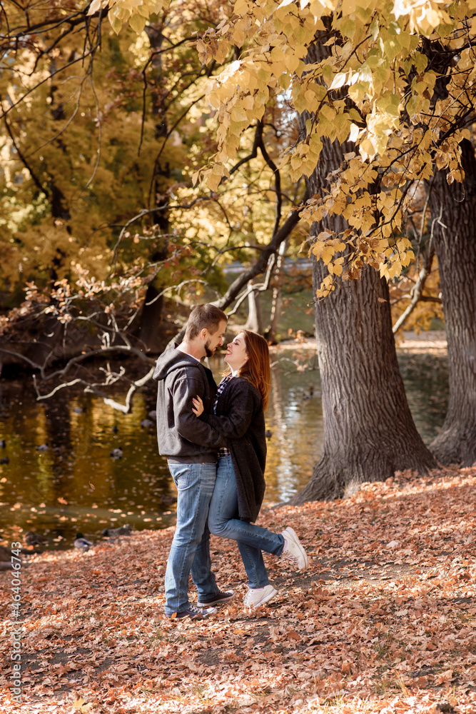 Beautiful young couple man and woman hugging in the park near the pond in leaf fall in autumn Beautiful young couple man and woman hugging in the park near the pond in leaf fall in autumn