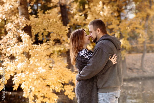 Beautiful young couple man and woman hugging in the park near the pond in leaf fall in autumn