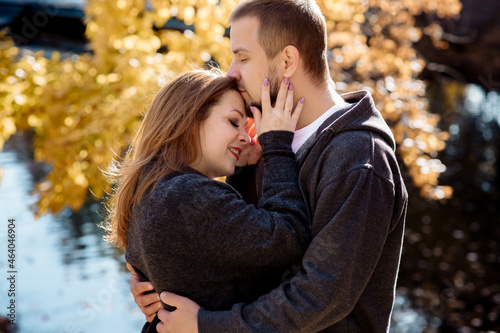 Beautiful young couple man and woman hugging in the park near the pond in leaf fall in autumn
