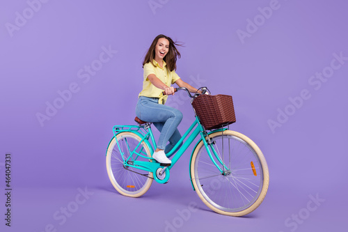 Full body profile photo of cute millennial brunette lady ride bicycle wear yellow top jeans shoes isolated on purple color background © deagreez