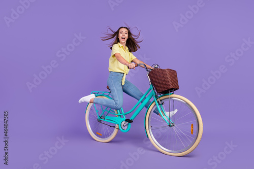 Fototapeta Naklejka Na Ścianę i Meble -  Full size profile photo of impressed young brunette lady go bicycle have fun wear yellow top jeans sneakers isolated on violet color background