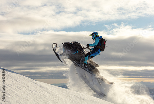 snowmobiler jumps in a bright helmet and overalls over a mountain valley after a snowfall on a frosty morning. snowmobile sports concept