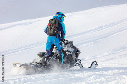 conquering the top on a mountain snowmobile with a body weight of one leg. snowmobiler harmoniously dressed in the color of a snow motorcycle