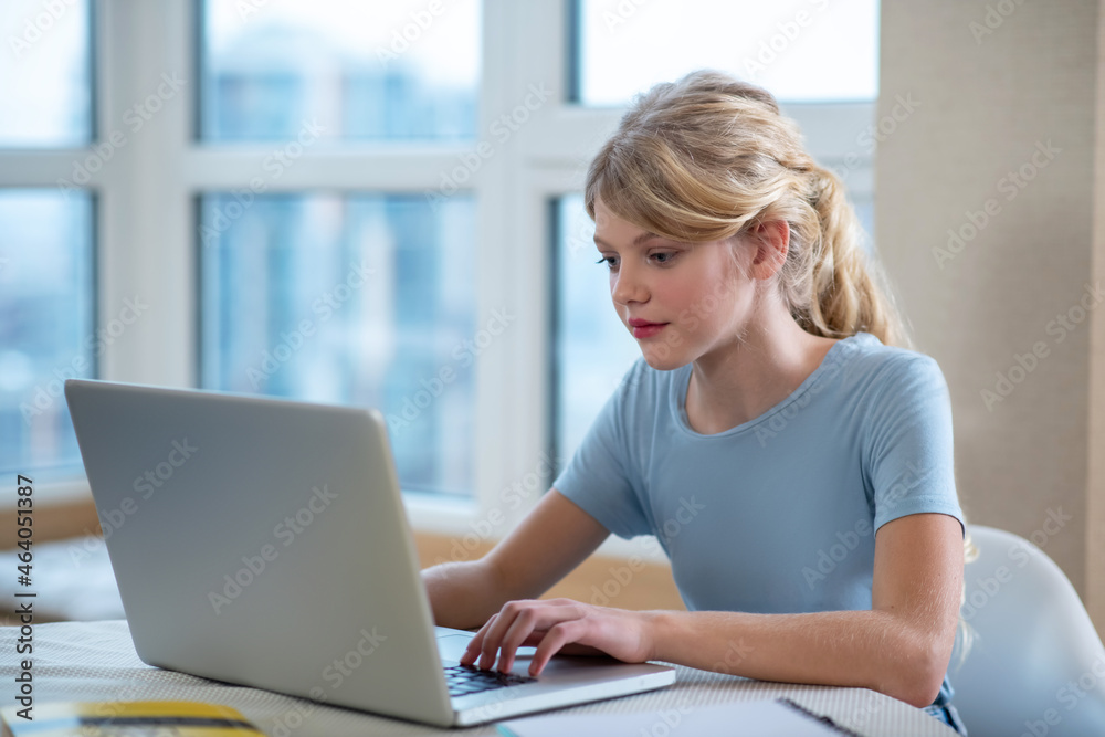 A pretty blonde girl sitting at the laptop and looking involved A pretty blonde girl sitting at the laptop and looking involved