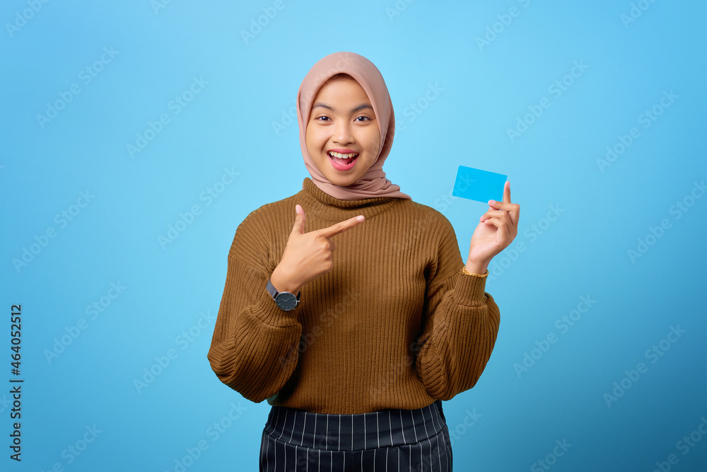 Cheerful young Asian woman pointing finger at credit card on blue background Cheerful young Asian woman pointing finger at credit card on blue background