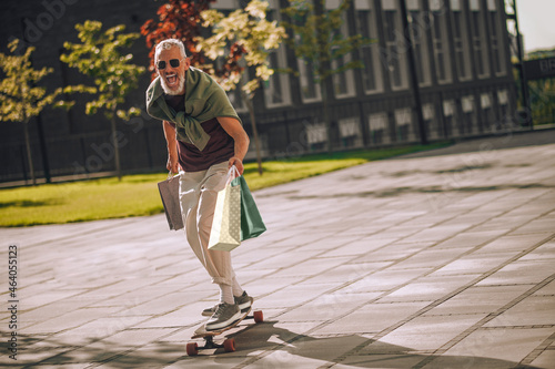 Fotografija Excited gray-haired bearded Caucasian man skateboarding outside