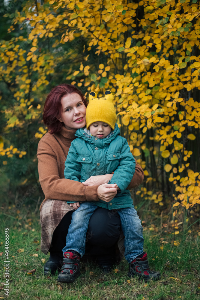 Little caucasian boy and his mother against yellow autumn forest