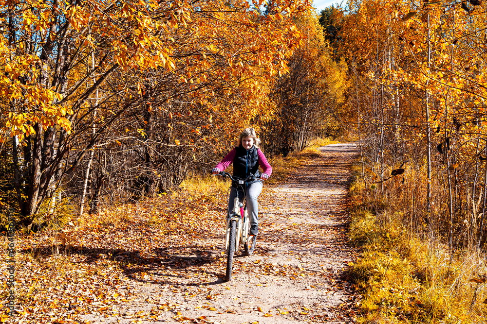 A girl rides a recreational bicycle through the park. Autumn leaves fall. A sunny autumn day.
