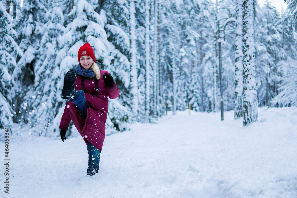 teenage girl in a red jacket kick the snow and laughing in a snowy forest
