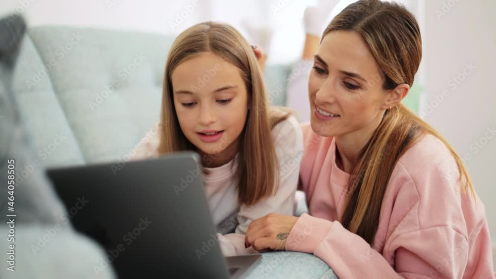 Positive daughter typing on laptop while her mom stroking her head at home Positive daughter typing on laptop while her mom stroking her head at home