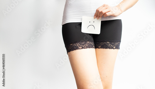 Young woman holds paper with sad above crotch on withe isolate background. Period Pain or vaginal or urinary infection female health Problem. Health Issues Concept.