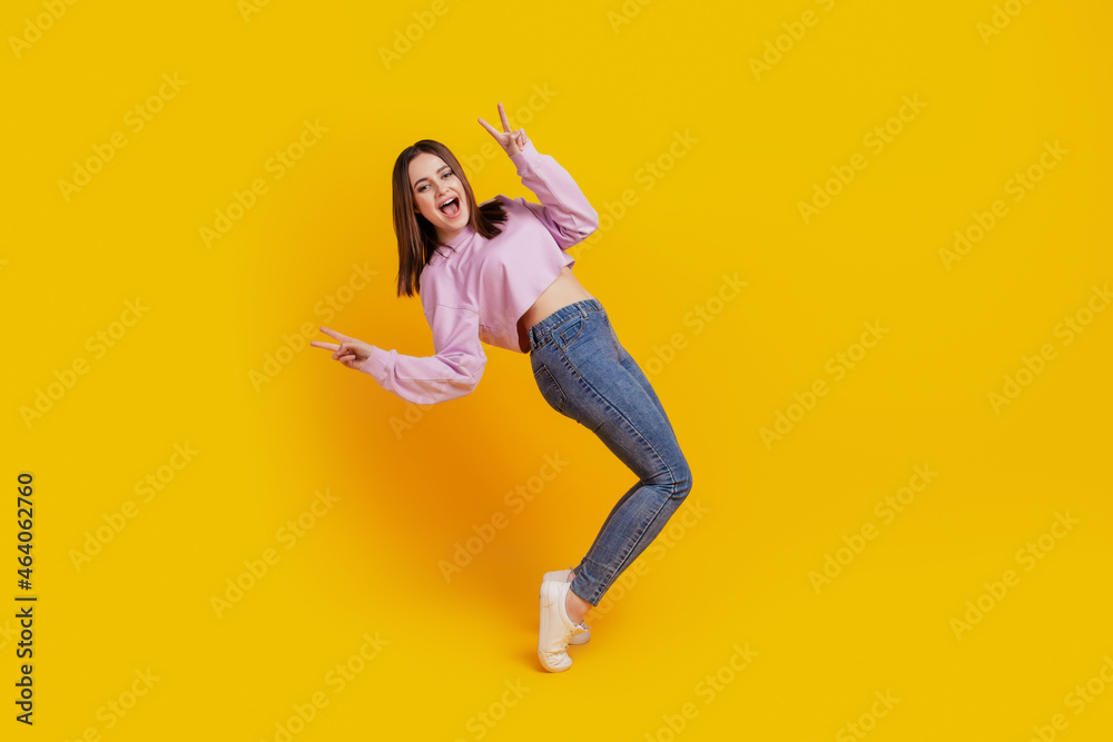 Full size profile side photo of young excited girl have fun show peace cool v-sign isolated over yellow color background